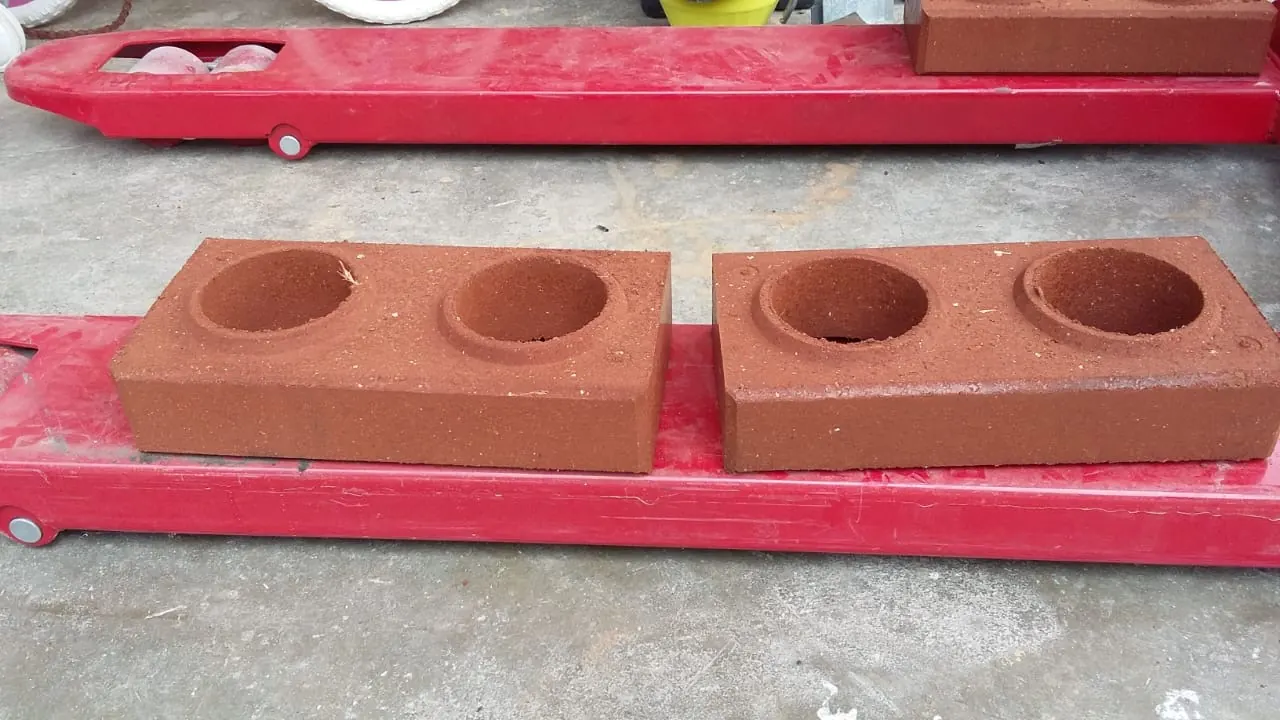 Dos ladrillos ecológicos color terracota con dos orificios cada uno, sobre una paleta de carga roja