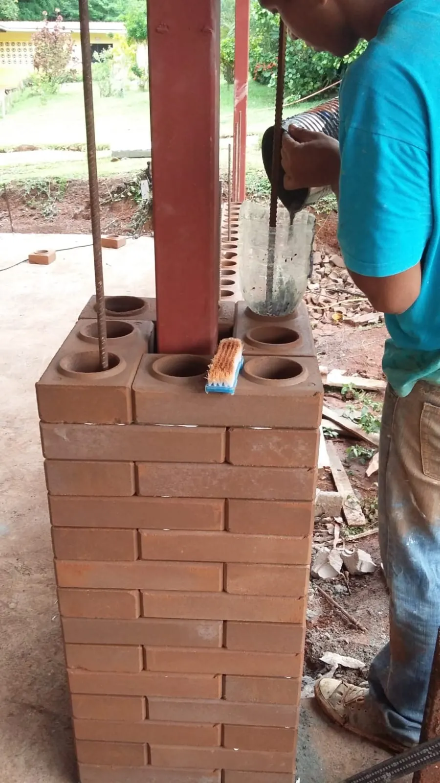Obrero vertiendo mortero por los orificios de una columna de ladrillo ecológico